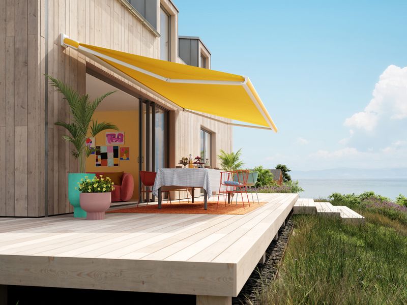 Side view of the MX-3 with a golden yellow awning cover from the Popart Edition mounted on a Scandinavian-style house.