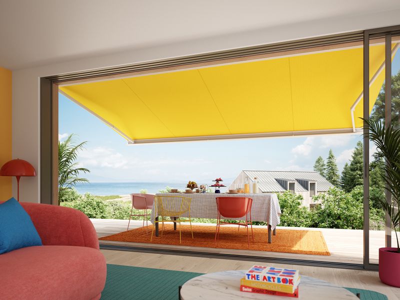 Udsigt fra et hus i skandinavisk stil til en terrasse dækket af en markise, MX-3 med et gult markisedæksel.