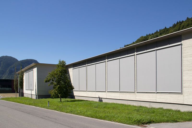Bâtiment à toit plat avec façade en bois, ombrage des fenêtres par store vertical markilux 710 en gris.