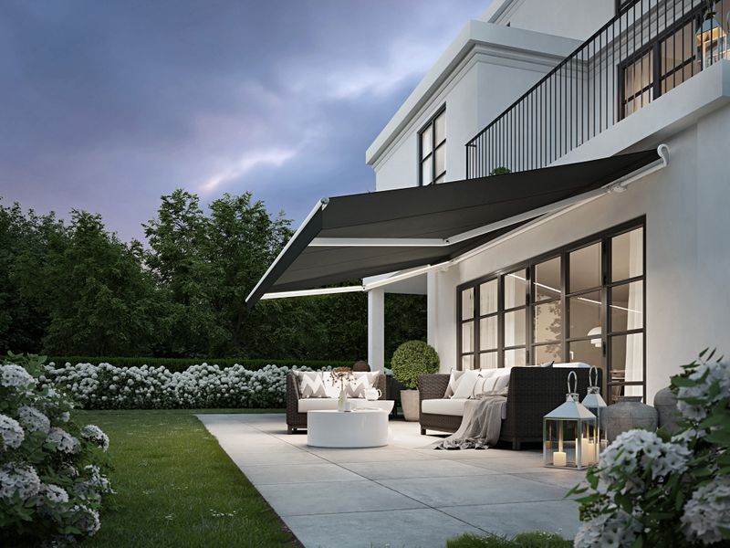 Villa urbaine blanche avec un store blanc markilux 1700 avec toile de store noire, l'éclairage dans les bras articulés et volant droit.