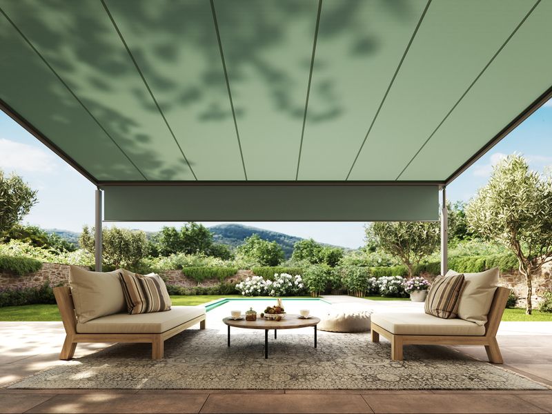 Toldo mx pergola cubic con armazón gris y lona del toldo verde sobre una terraza. El mobiliario de exterior crea un ambiente relajado y el Súper-sombra proporciona abundante sombreado.