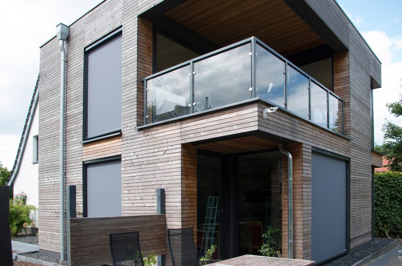 Single-family house with wooden facade and gray markilux vertical blaind window awnings.