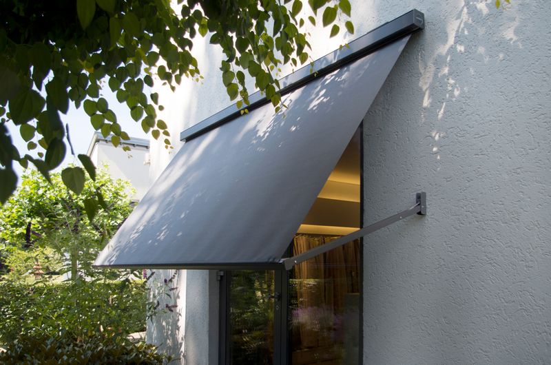 Gray drop-arm cassette awning markilux 730 in front of a window.