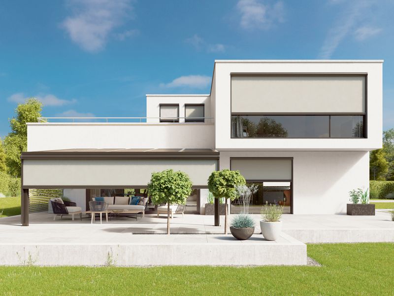 Vue de face d'une maison blanche moderne avec jardin. La maison a de très grandes fenêtres sur lesquelles ont été fixés les stores verticaux mx 879 et mx 876 avec toile de store en tissu de couleur crème.