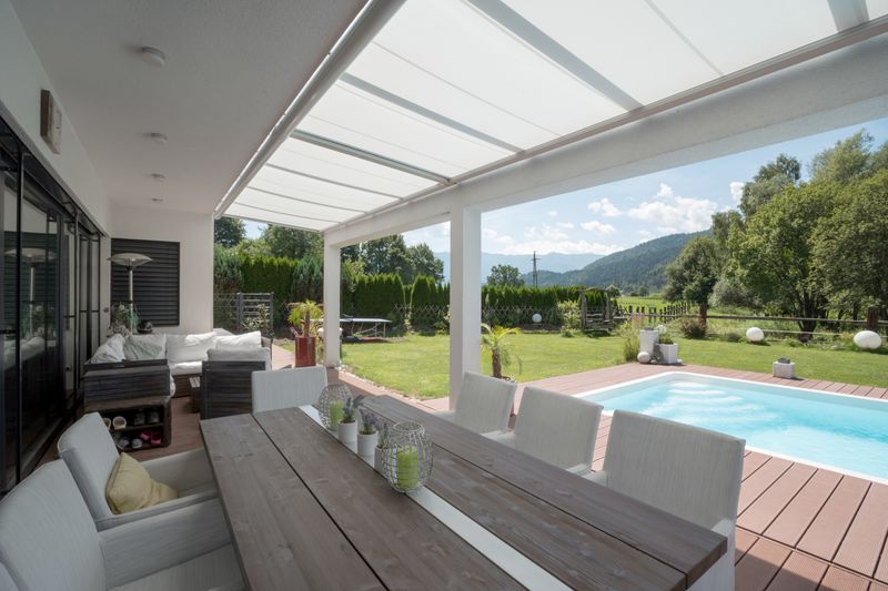 Terrace shaded with white under-glass awning markilux 879, pool and mountains in the background.