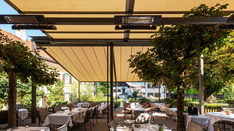 Vue sur une terrasse de restaurant couverte par des stores peroglamiques markilux avec radiateurs thermiques.