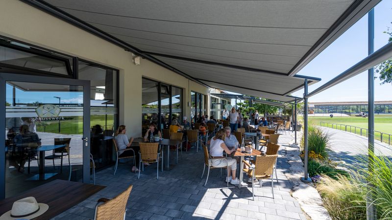 Imagen de referencia de varios toldos clásicos de pérgola de color antracita sobre una zona de restaurante al aire libre.