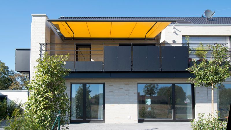 Markilux 5010 (moldura cinzenta, cobertura de tecido amarelo) cobre uma varanda.