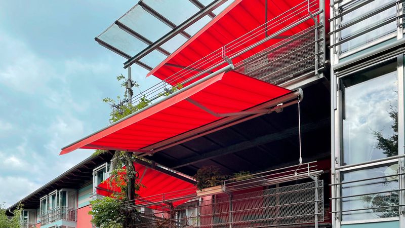 Varios toldos markilux 1710 con lona de rayas rojas y volante para dar sombra a algunos balcones.