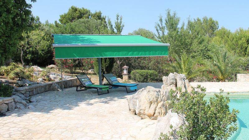 Sombra do toldo markilux planet com tecido verde e shadowplus numa piscina mediterrânica.
