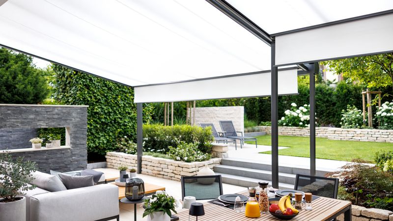 Moderna terrazza con zona pranzo e salotto, coperta da una combinazione di tetto nero della vostra terrazza e tenda sottovetro bianca con Ombrissima.