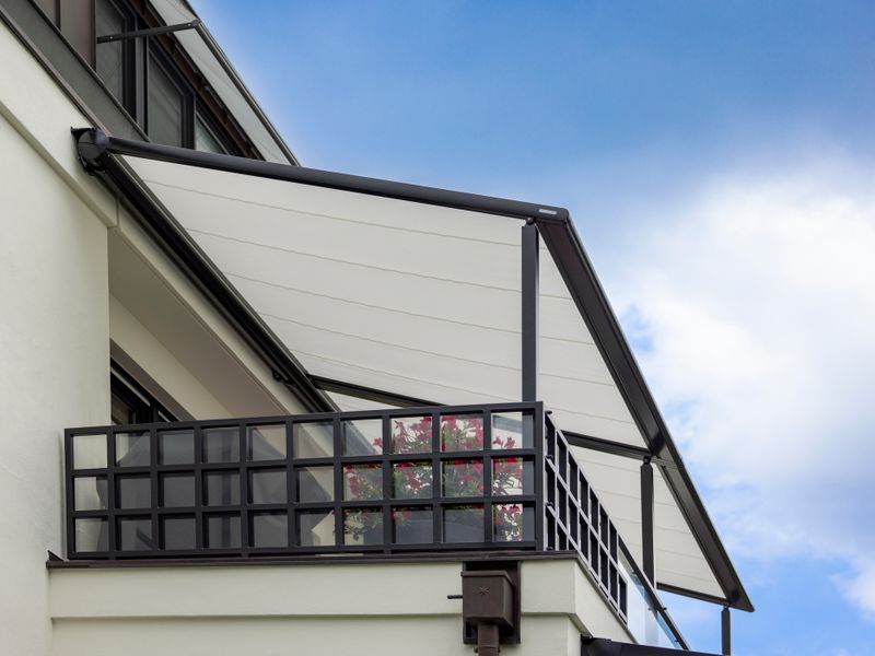 Side view of a pergola awning on the balcony of a modern house. White and black color scheme to match the house.