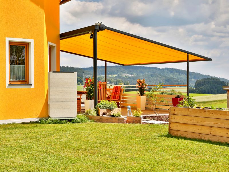 Yellow house with terrace covered by a markilux pergola awning with yellow fabric cover.