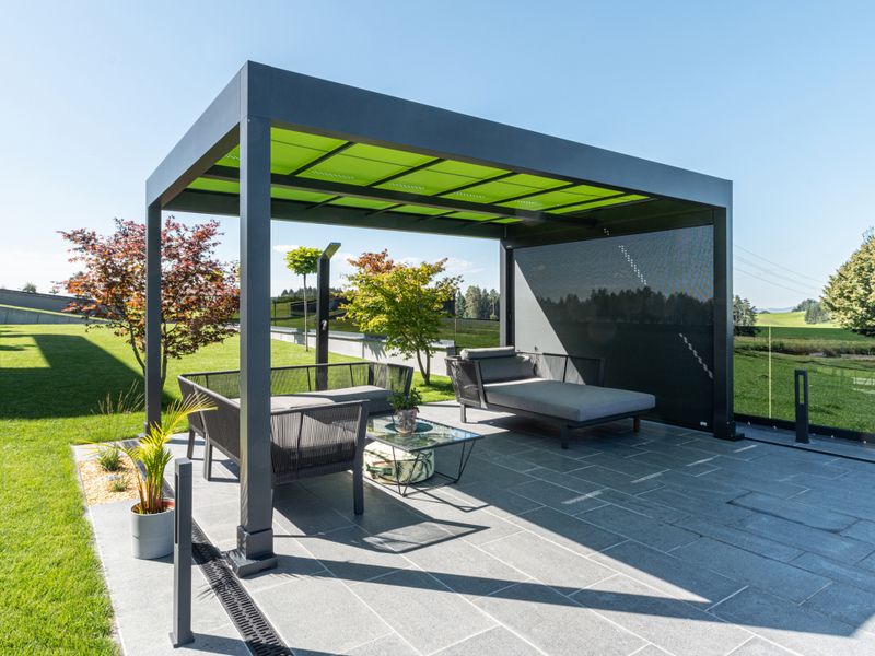 Reference of a freestanding patio cover markilux markant with green awning cover and vertical blind with gray translucent awning cover, on a patio away from the house.
