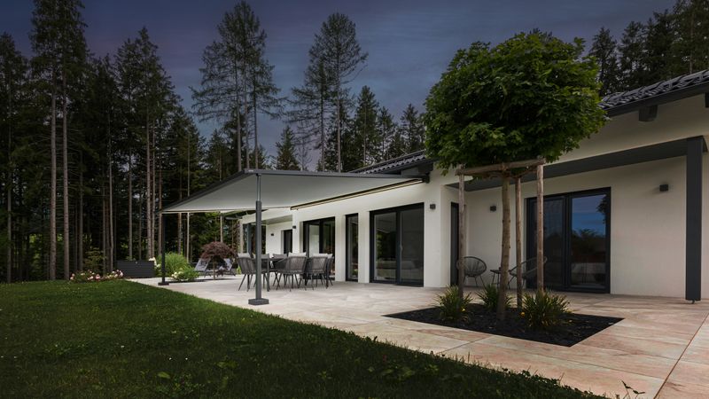 Store de pergola markilux pergola style sur un grand bungalow, éclairé la nuit.
