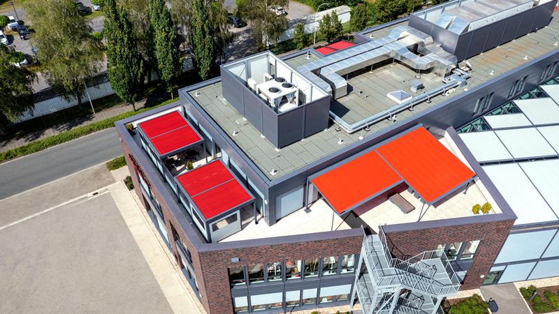 Immagine di riferimento di tenda da sole con telo rosso sulla terrazza dell'edificio markilux a Emsdetten.