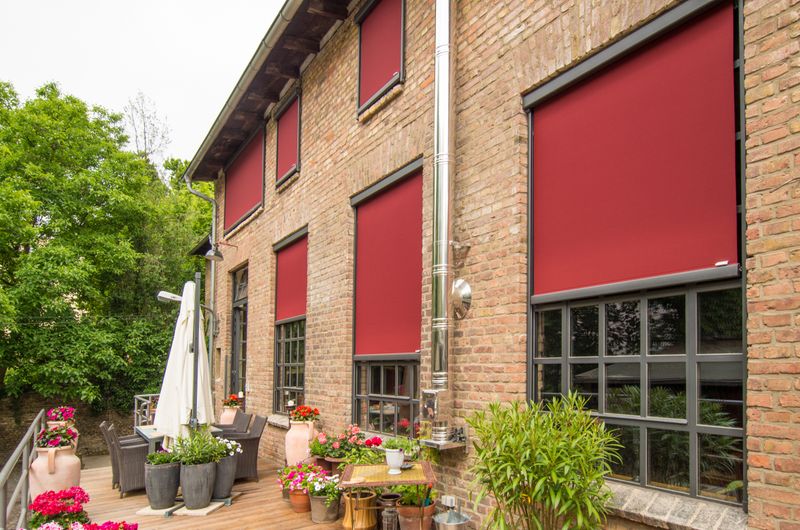 Bâtiment en briques, de type loft, avec des fenêtres verticales markilux rouges