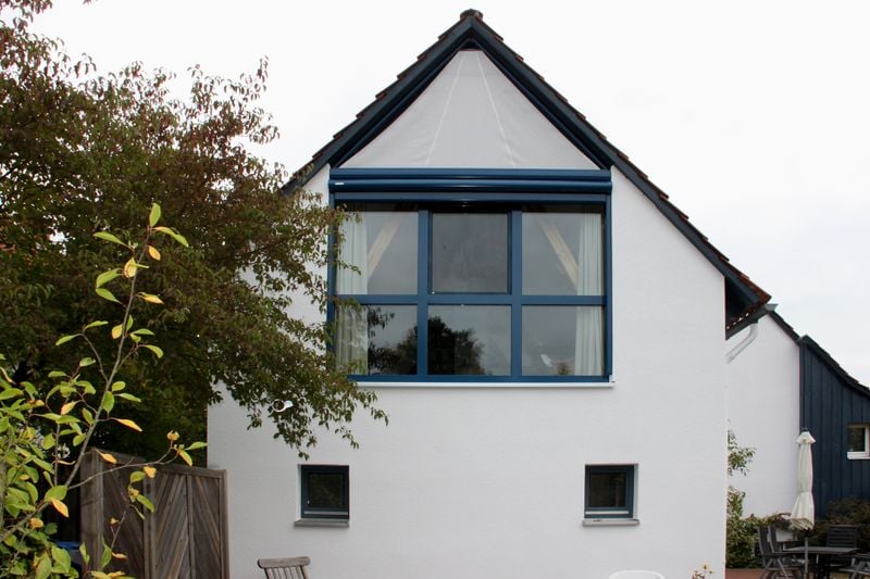 Maison blanche avec fenêtre à pignon triangulaire, store de fenêtre étendu markilux 893, triangulaire.