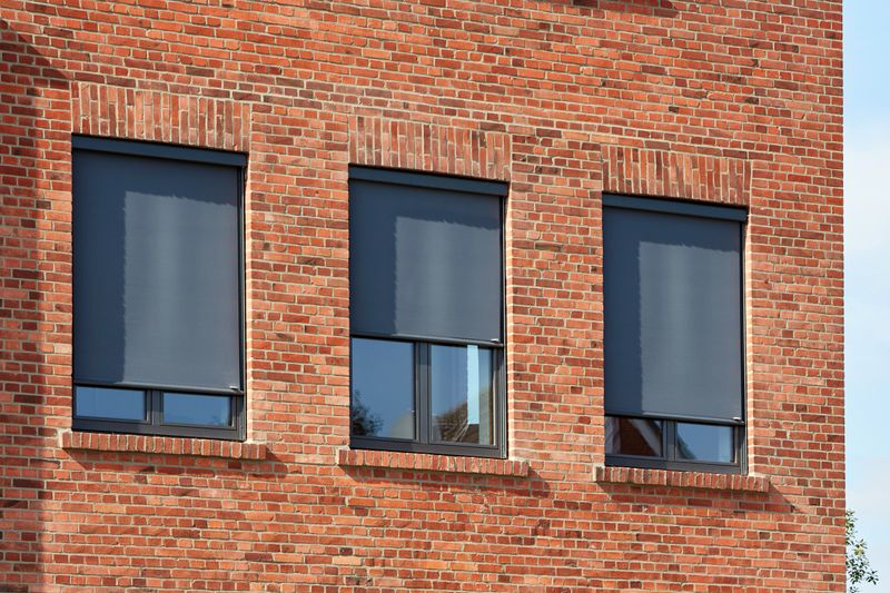 Objecto de referência: edifício de tijolo com persianas verticais markilux 620 com cobertura de tecido cinzento.