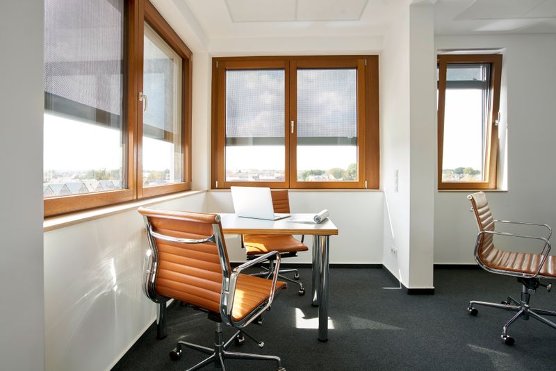 Referenceobjekt: skrivebord i en kontorbygning i umiddelbar nærhed af vinduer, som har en markise markilux 620 med grå gennemsigtig stofbetræk.