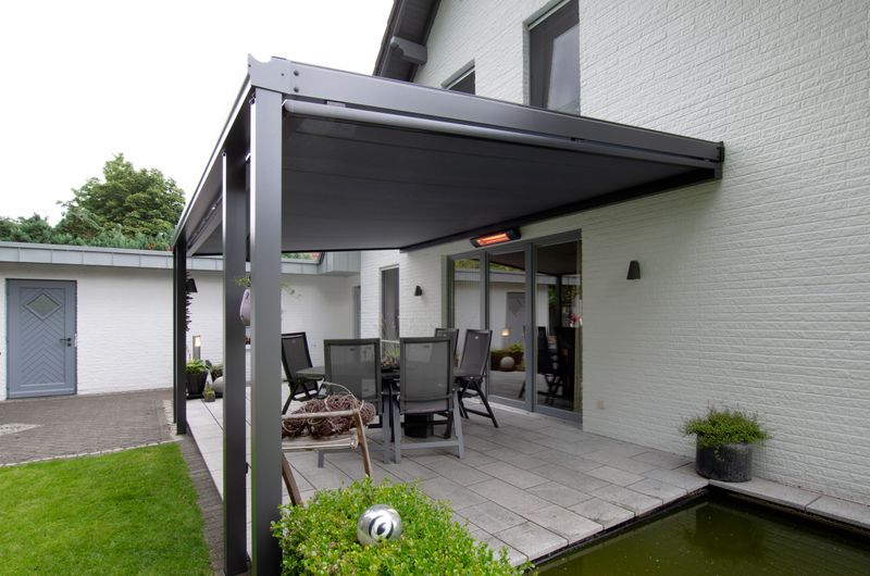 White house with small terrace and pond. The terrace is covered by a dark gray patio roof with color-coordinated under-glass awning markilux 779. Additional equipment heat radiator.