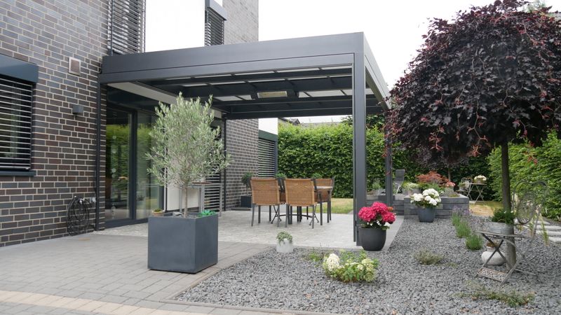 Referencia de una cubierta de patio independiente markilux markant con lona del toldo de luz para cubrir un patio en una casa de ladrillo gris.