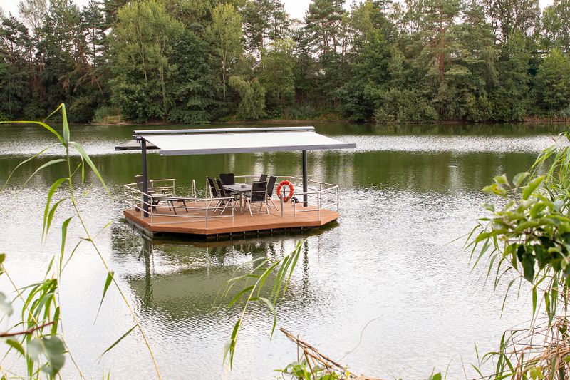 markilux syncra avec des stores à cassette markilux 970 avec une toile beige des deux côtés, installés sur une petite terrasse en bois en îlot dans le lac.