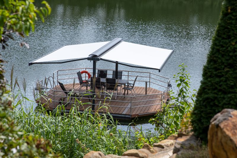 markilux syncra con toldos cofre markilux 970 con tejido cofre beige a ambos lados, instalado en una pequeña terraza de madera isla en el lago.
