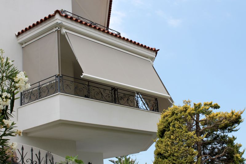 Combinação de estore vertical e toldo de braço rebatível para sombrear uma varanda, esquema de cores bege.