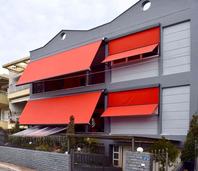 Referenzbild: Graues Haus mit zwei ausgefahrenen roten Kassettenmarkisen markilux 6000 neben jeweils einer roten Markisolette markilux 740.