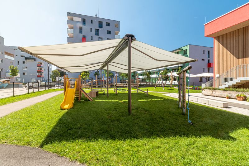 Doppia tenda da sole markilux 1600 con telo della tenda da sole fissato al sistema di intelaiatura markilux syncra. La tenda da sole ombreggia il parco giochi di un asilo.
