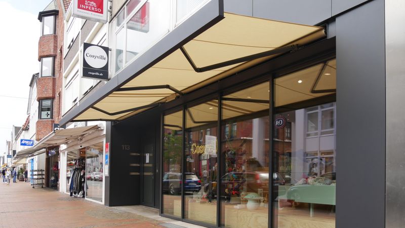 Lona toldo cofre markilux 3300 acoplada con tejido beige en el diseño de la fachada negra de una tienda.